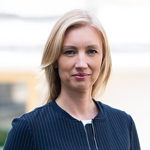 Woman with fair hair in a professional attire is smiling outdoors.