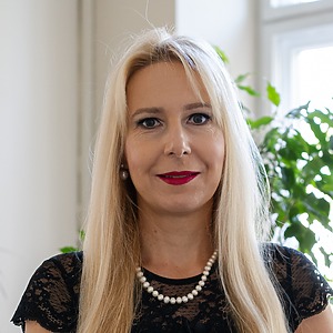 Smiling woman with blonde hair wearing a black blouse in a office.